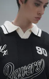 Sweater de punto negro con cuello polo en color crema, manga larga y diseño oversize. Presenta bordados en el frente con la inscripción 'Ravers', el número '90' y letras cursivas, con terminaciones en punto rib en puños y cuello.