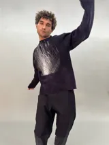 Buzo de lana merino afieltrada color negro con estampado abstracto plateado en el frente. Tiene cuello redondo y puños con forma que cubre levemente la mano. Es más largo en la parte inferior trasera.