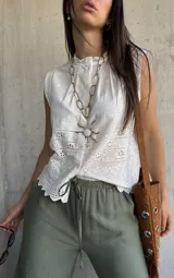 Camisa sin mangas blanca de broderie, con cuello alto fruncido y cierre frontal con botones.