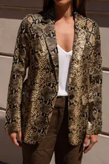 Blazer de corte sastrero con estampado de piel de serpiente en tonos grises y negros. Presenta solapas clásicas, cierre frontal con botones y mangas largas con detalle de botones en los puños.