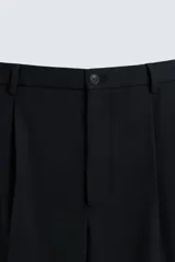 Pantalón negro de corte recto (regular fit) confeccionado en tejido compacto. Presenta pliegues frontales marcados, cierre frontal con botón y cremallera, y bolsillos de vivo en la parte trasera.