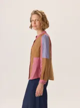 Camisa de algodón con diseño de bloques de color en tonos marrón, rosa y lila. Presenta cuello redondo, cierre frontal con botones y mangas largas.