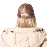 Gorra tipo béisbol confeccionada en cuero sintético color marrón con efecto desgastado y costuras decorativas en contraste.