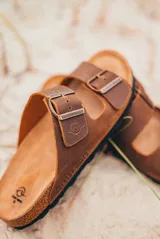 Sandalias marrones de cuero con plantilla de corcho, suela negra y doble tira con hebilla metálica ajustable.