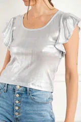 Remera de tela metalizada color plateado, con cuello redondo y mangas cortas con volados. Presenta un diseño ajustado al cuerpo y acabado brillante.