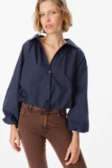 Camisa de corte holgado color marrón chocolate, con cuello clásico, cierre frontal de botones y mangas largas abullonadas con frunces en los hombros.