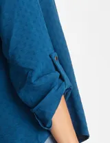 Blusa de color blanco con escote en V y cuello mao. Presenta mangas largas con presilla y botón para regular el largo, y un corte holgado con ruedo redondeado.