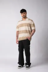 Remera tipo chomba de tejido de punto con diseño de rayas horizontales anchas en tonos beige y crema. Presenta cuello polo con escote en V, mangas cortas y un corte holgado oversize.