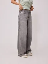 Jean de corte baggy y tiro medio, confeccionado en denim de algodón en tono azul claro con efecto lavado. Presenta diseño de cinco bolsillos, cierre frontal con botón y cremallera, y pernera ancha.