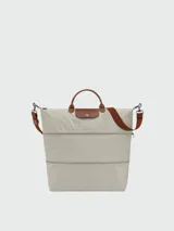Bolso de viaje Longchamp modelo Le Pliage Original, de diseño ampliable, confeccionado en nylon negro con detalles en cuero marrón en las asas y solapa frontal con cierre de botón a presión. Incluye correa ajustable y extraíble.