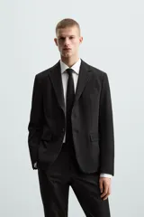 Blazer slim fit de color negro, confeccionada en tejido con viscosa. Presenta cuello con solapas de muesca, cierre frontal con botones, bolsillo de vivo en el pecho y bolsillos de solapa en la cadera.