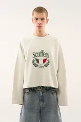 Buzo de corte boxy color crudo, con cuello redondo y mangas largas de hombros caídos. Presenta un estampado frontal con el logo de la marca, un escudo con los colores de la bandera italiana y detalles de laureles.