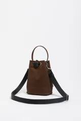 Bolso tipo bucket mini de Bimba y Lola, confeccionado en gabardina color marrón. Cuenta con cierre de cordón ajustable, bolsillo frontal externo, asa de mano superior y correa de hombro ajustable. Presenta el logo de la marca estampado en el frente.