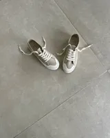 Zapatillas urbanas de lona color beige con cordones blancos y suela de goma blanca con diseño geométrico.