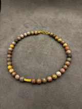 Collar corto de piedras volcánicas marrones y marrones oscuras, con detalle cilíndrico dorado en el centro.
