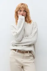 Sweater de punto en color beige melange, con cuello redondo y mangas largas. Presenta un diseño decorativo con perlas aplicadas en la parte frontal y en las mangas.