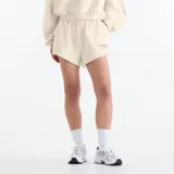 Short New Balance de felpa francesa color beige, con cintura elástica y cordón de ajuste. Cuenta con bolsillos laterales y detalle de bordado y estampado con el logo de la marca en el muslo izquierdo.