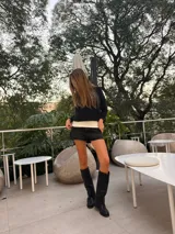 Botas de caña alta confeccionadas en ecocuero negro, con diseño de tres hebillas metálicas laterales y suela plana.