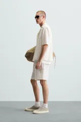 Bermuda de algodón color blanco, de corte relajado (relaxed fit), con cintura elástica ajustable mediante cordón. Posee bolsillos laterales y un bolsillo trasero de plastrón. Presenta un bordado en contraste en la pernera.