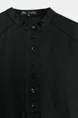 Camisa de cuello redondo y manga corta abullonada, color negro, de corte recto con aberturas laterales y cierre frontal con botones. Perteneciente a la colección ZARA Woman Collection.