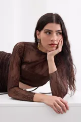 Top de encaje color marrón con transparencias sutiles, cuello redondo, mangas largas y espalda descubierta con delicados lazos ajustables.