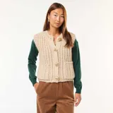 Chaleco de punto beige con textura de ochos, sin mangas, con cuello redondo y cierre frontal con botones grandes dorados.