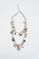 Collar de doble cadena plateada con múltiples dijes colgantes de diversos estilos, incluyendo corazones, cruces, figuras geométricas, cuentas de colores y elementos metálicos variados.