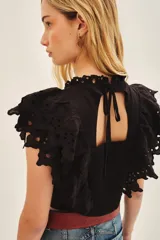 Camisa corta de voile de algodón negro, con escote redondo y mangas con volados decorados con puntilla de algodón bordada.