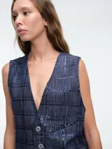 Chaleco sastrero de denim negro con diseño de cuadros y aplicación de lentejuelas sutiles. Presenta escote en V, cierre frontal con botones metálicos y bolsillos delanteros.