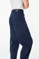 Jean de corte balloon en color azul marino, con cintura alta, cierre frontal con botón y bolsillos laterales. Presenta costuras laterales curvadas que definen su silueta amplia y relajada.