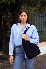 Bolso negro de cuero gamuzado con correa larga regulable y logo de la marca grabado en el frente.