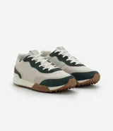 Championes de estilo jogging con diseño de paneles en tonos beige y verde oscuro. Presentan una combinación de malla técnica y refuerzos en material sintético, con suela dentada en color marrón y entresuela blanca.