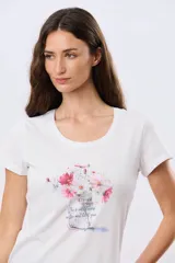 Remera blanca de manga corta y cuello redondo, con estampa frontal de flores en tonos rosados dentro de un frasco de vidrio y detalles de letras bordadas.