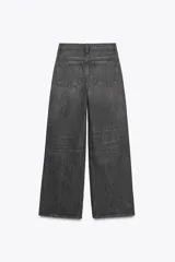 Jeans de tiro alto, color gris oscuro lavado, con pierna ancha extra larga (full length) y diseño de cintura cruzada asimétrica con cierre frontal de cremallera y botones metálicos.