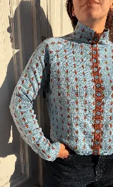 Cardigan reversible de punto con estampado de rombos pequeños, cuello alto y cierre frontal completo con botones. Presenta detalles de ribetes en color contrastante en cuello, puños y cartera de botones.