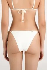 Calzón de bikini color crema con tiras laterales ajustables y detalles de cuentas metálicas doradas en los extremos.