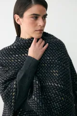 Ruana tejida artesanalmente en lana, con diseño de textura tramada en tonos oscuros con detalles en colores tierra. Presenta un cuello alto y mangas integradas de punto liso.
