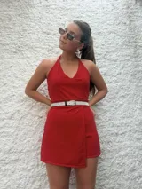 Mono corto color rojo con escote halter y espalda descubierta. Presenta corte a la cintura y falda cruzada tipo pareo.