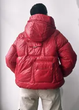 Campera puffer roja con capucha, bolsillos frontales y cordón ajustable en el ruedo.
