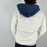 Canguro blanco hueso de algodón con felpa, capucha forrada en azul marino, cierre parcial con cremallera, cordón ajustable y bolsillo tipo canguro con solapa.