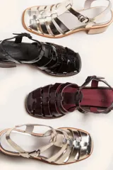 Sandalia plateada de cuero con tiras entrecruzadas, taco de madera y hebilla lateral.