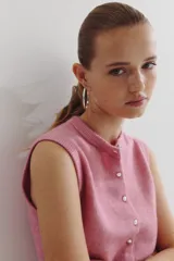 Chaleco corto de punto suave color rosado, con cuello redondo y cierre frontal de botones metálicos.