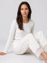 Pijama de dos piezas compuesto por una remera de manga larga y pantalón largo, confeccionado en tejido suave de color blanco con detalles de encaje en la cintura y en el ruedo del pantalón.