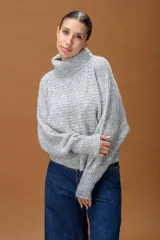 Sweater de punto con cuello alto, manga larga y diseño holgado. Presenta una textura suave con un sutil acabado brillante.
