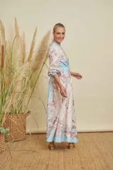 Vestido largo estampado con motivos florales en tonos pastel y detalles de cadenas doradas. Presenta cuello mao, cierre frontal con botones variados, mangas largas con puños elásticos y un cinturón a tono con hebilla dorada que realza la cintura. El ruedo del vestido tiene una franja de color celeste.