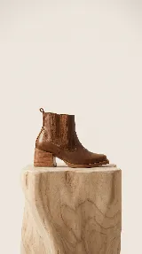Bota corta tipo chelsea de cuero color suela, con paneles laterales de gamuza al tono y taco cuadrado foliado en madera de 6 cm.