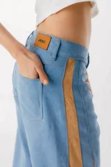 Pantalón de jean azul oscuro de pierna ancha y tiro medio, con paneles laterales en contraste de color marrón. Presenta costuras pespunteadas en tono tostado y terminación desmechada en el bajo.