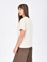 Remera lila de corte recto y mangas cortas, con estampado pequeño de un gato blanco con gorro rojo, gafas de sol y copa de vino, junto a la frase 'J'adore'.