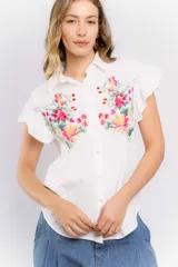 Camisa blanca de mangas cortas con volados y bordado de flores en el frente.