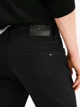Jean negro Tommy Hilfiger modelo Harlem de corte recto, con cierre de cremallera y botón, diseño de cinco bolsillos, detalles distintivos de la marca y logo bordado en el bolsillo trasero.
